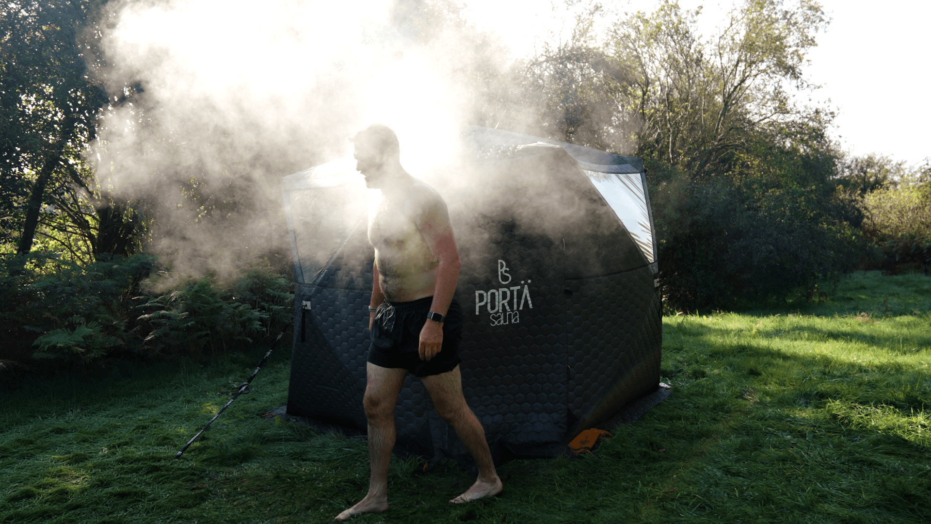 Person stepping out of a steaming sauna tent in a lush green field
